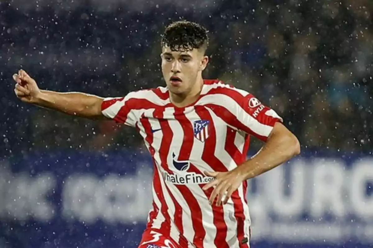 A football player in an Atlético de Madrid uniform in the middle of a match in the rain.