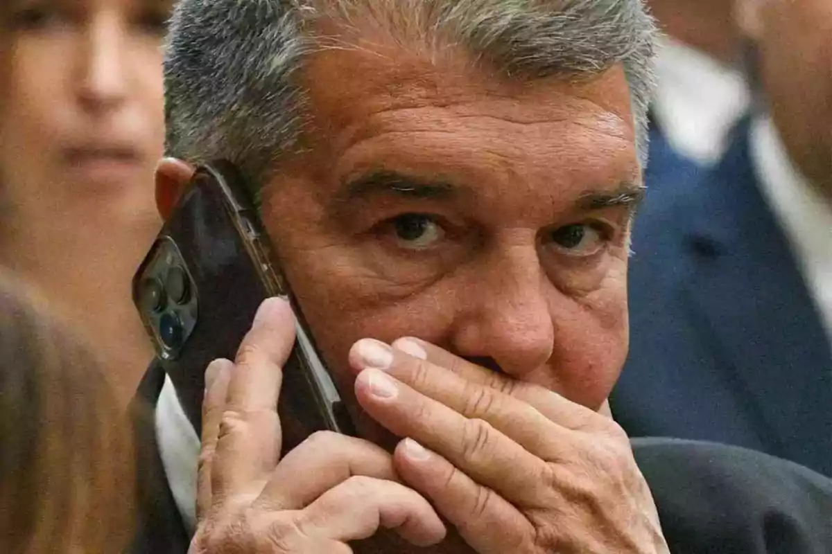 Gray-haired man talking on the phone and covering his mouth with his hand.