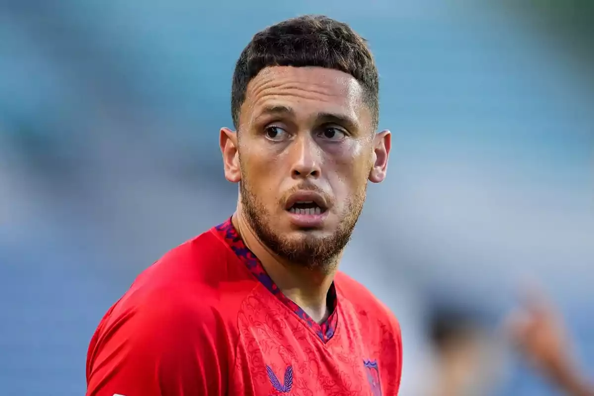 A football player in a red jersey looking to the side in a stadium.