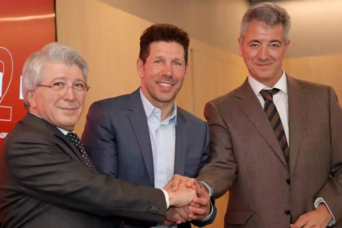 Three men in suits shaking hands and smiling at an event.