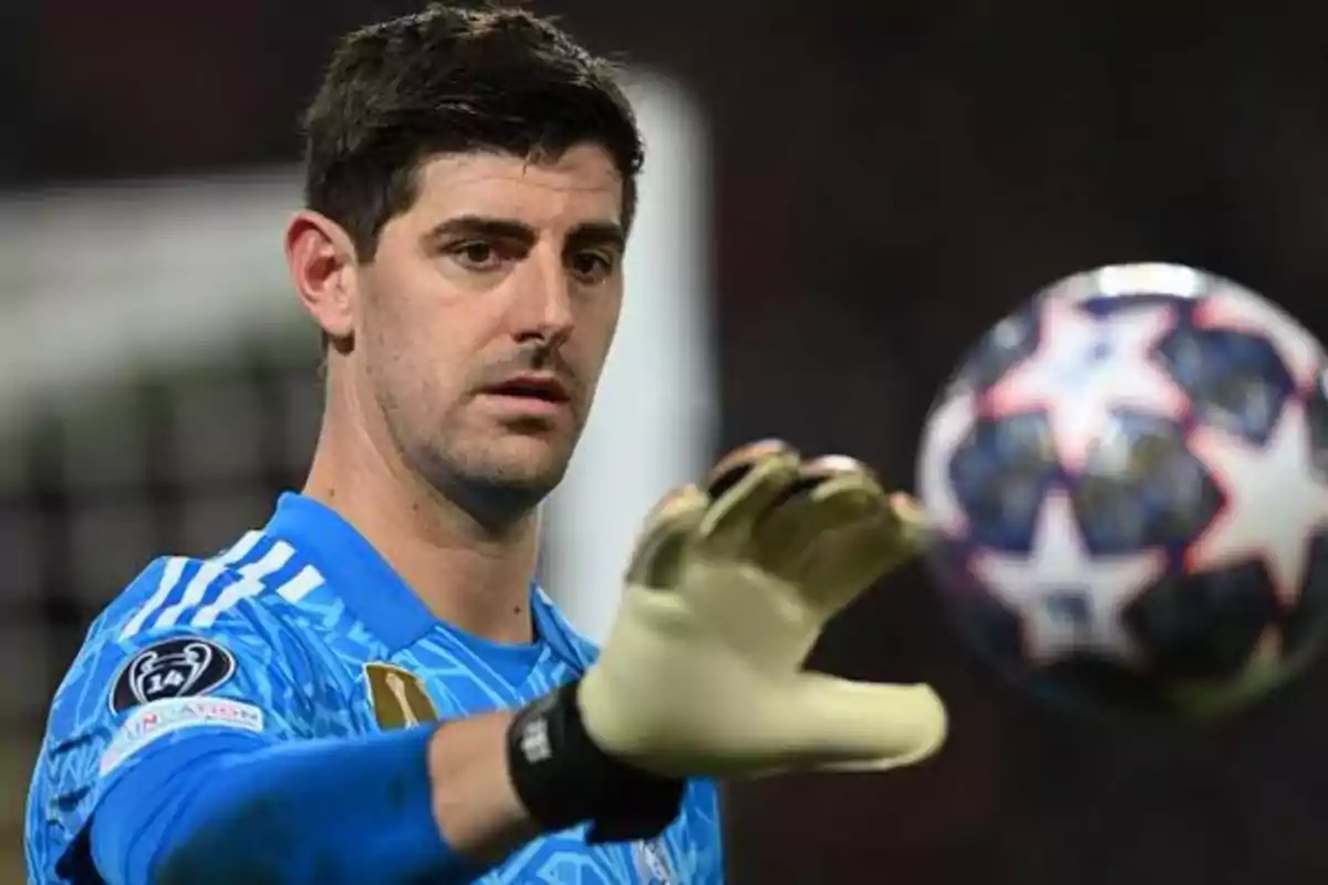 A soccer goalkeeper in a blue uniform and gloves looks at a soccer ball.