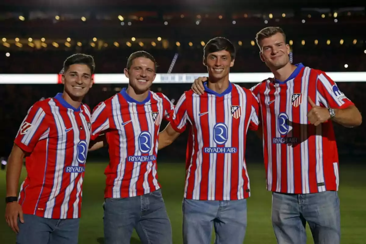 Four men wearing Atletico Madrid shirts posing together in a stadium.