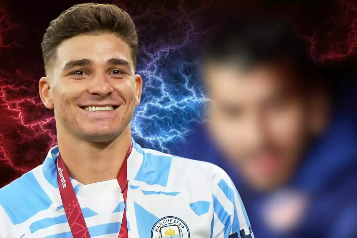 A football player smiles as he wears a Manchester City medal and shirt, against a background of red and blue rays.