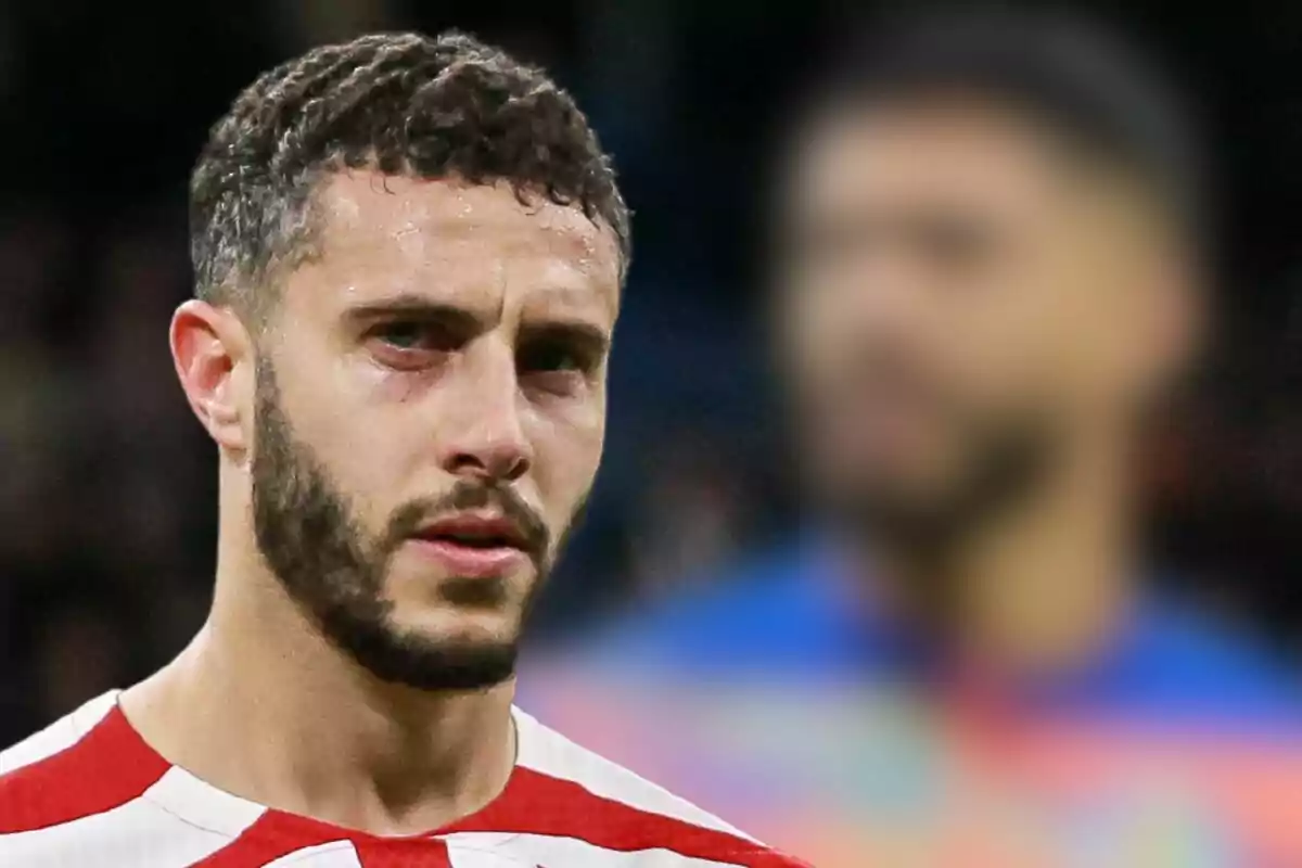 Football player in red and white striped shirt in foreground, with another player out of focus in background.