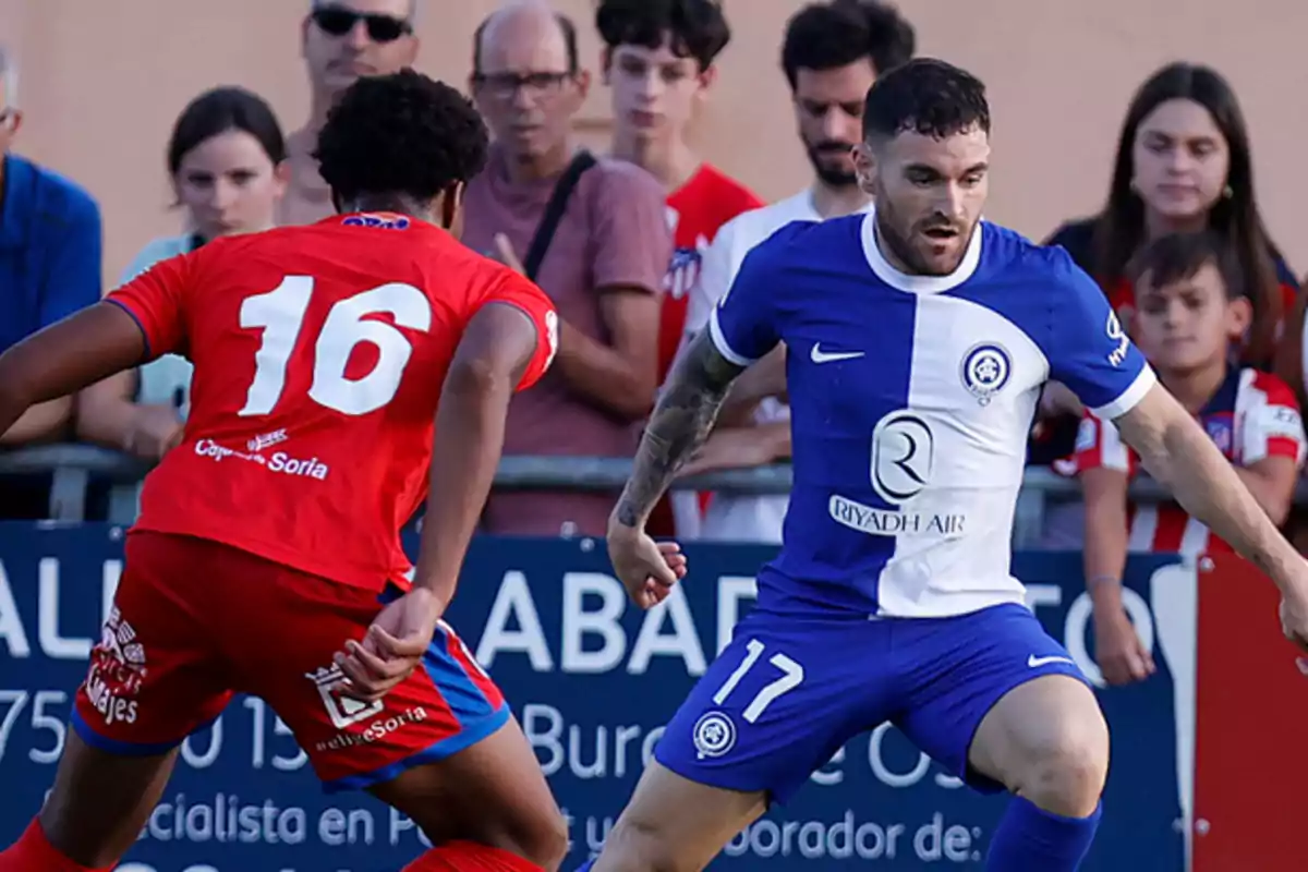 Two soccer players compete for the ball while the public watches from the stands.