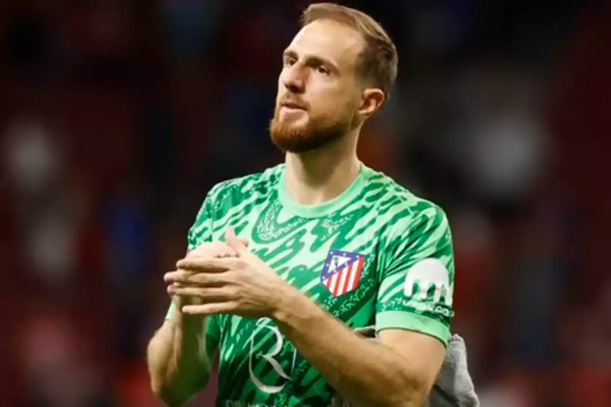 A football player in a green Atlético de Madrid uniform applauding in a stadium.