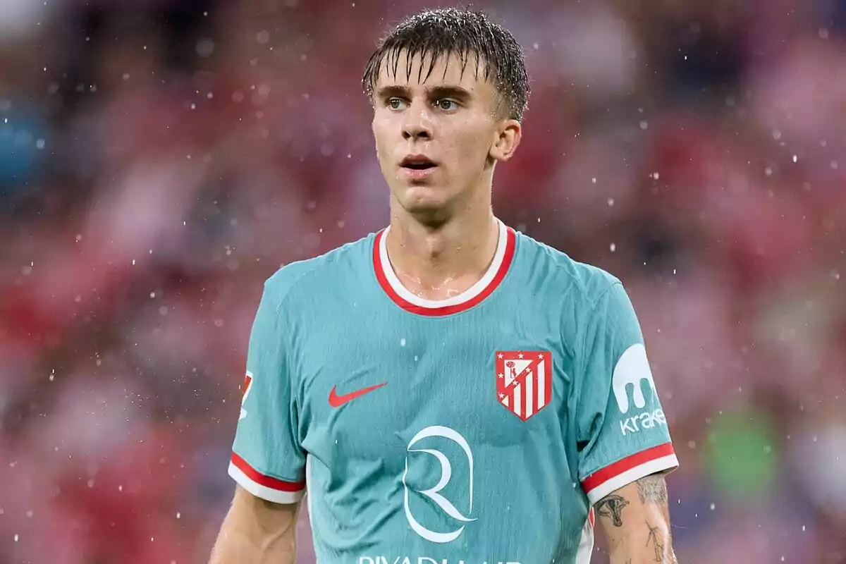 Football player wearing an Atlético de Madrid shirt at a match in the rain.