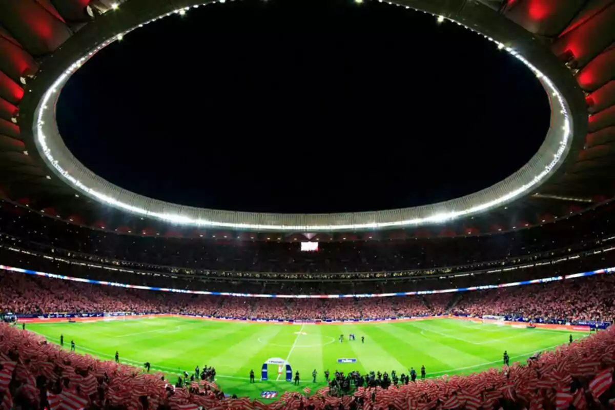 Illuminated football stadium during a night match with fans in the stands.