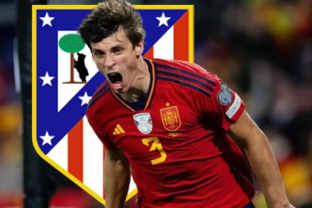 A soccer player wearing the Spanish national team shirt shouting with the Atlético de Madrid shield in the background.