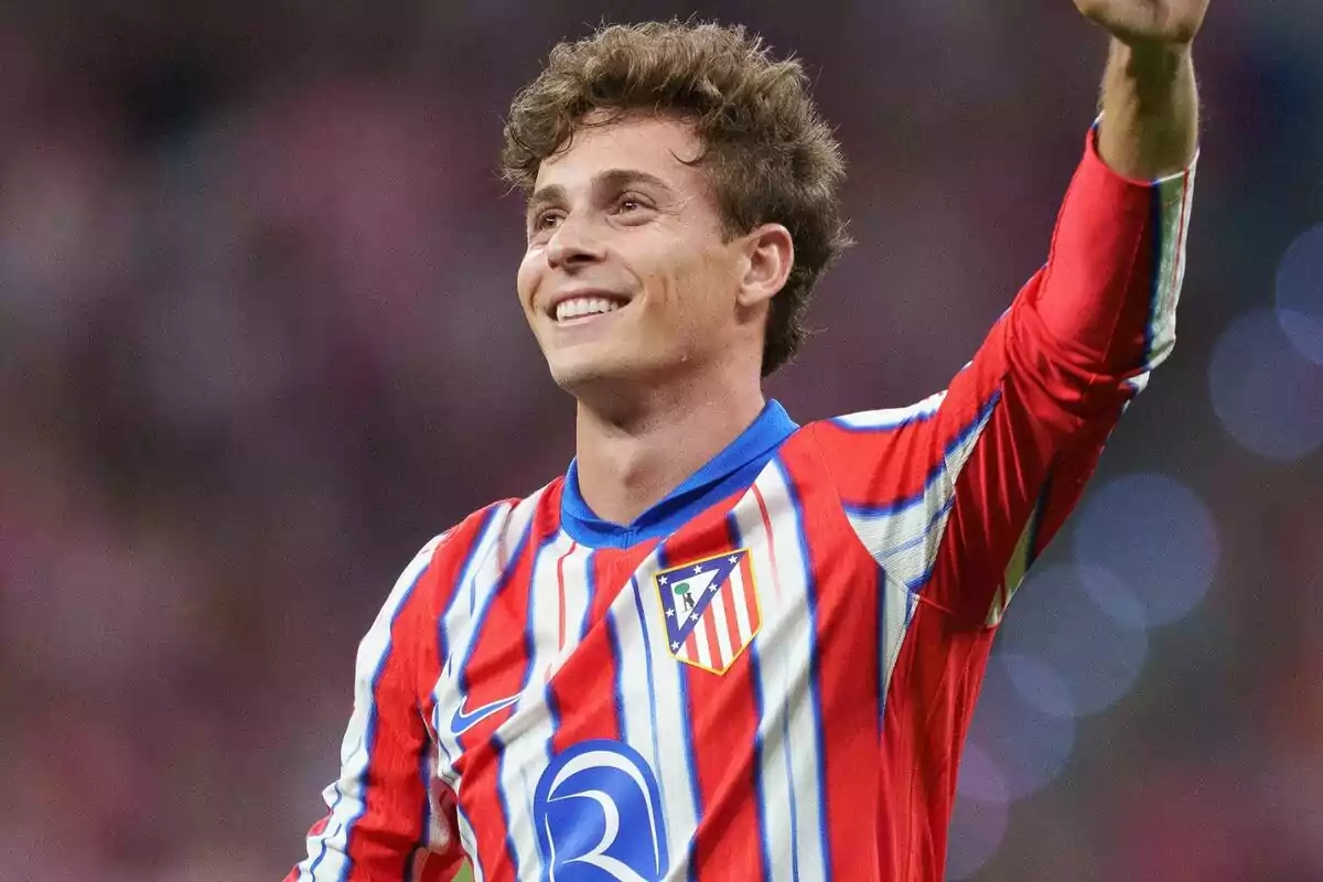 Football player wearing Atlético de Madrid shirt smiling and raising his hand.