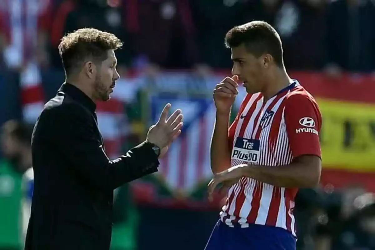 A football coach talking to an Atlético de Madrid player on the pitch.