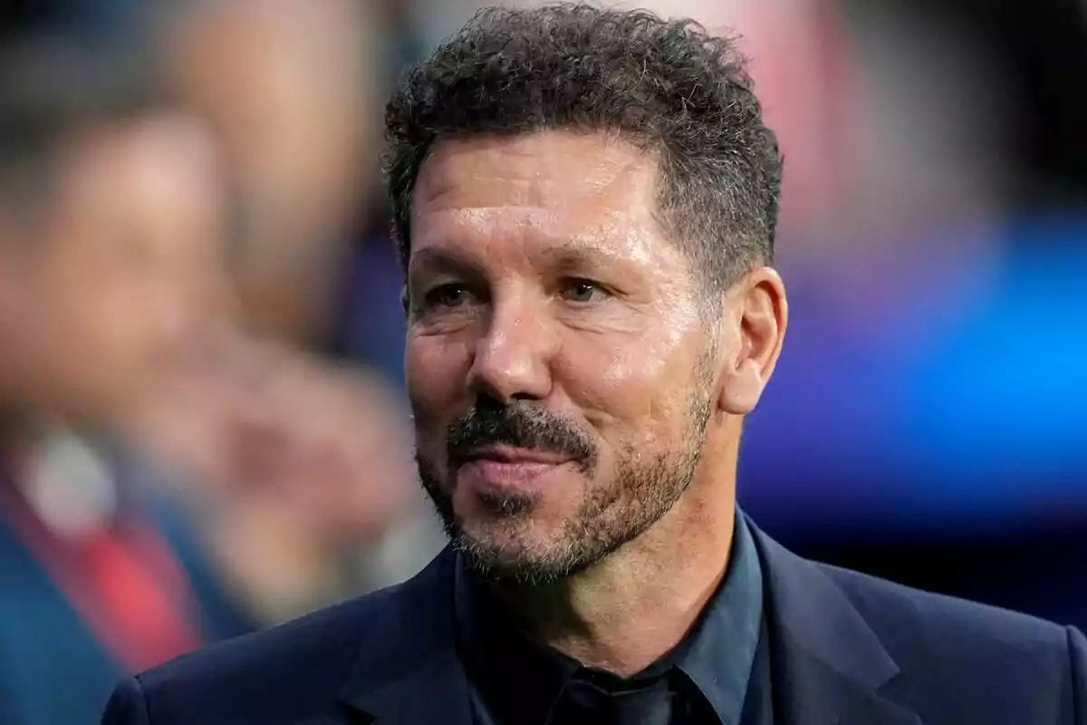 Man with beard and curly hair, dressed in a dark suit, smiling.