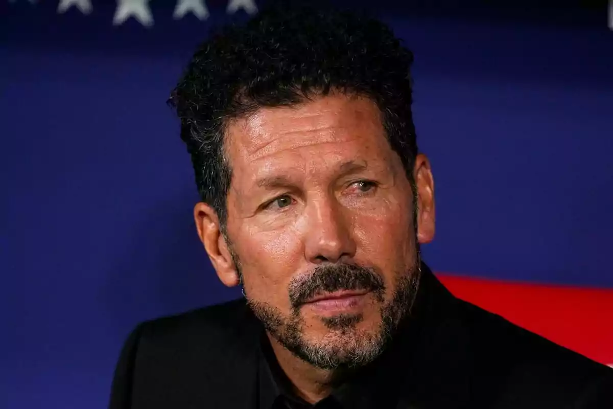 Curly haired man with beard looking to the side with serious expression, blue background with white stars.